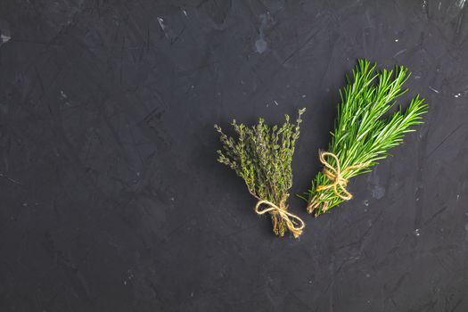 Rosemary and thyme bunches of bouquets on black stone concrete textured surface background. Top view with copy space for your text.