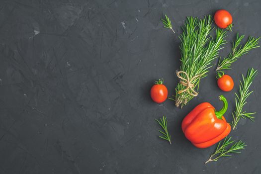 Rosemary bunch of bouquets, raw pepper and cherry tomatoes on black stone concrete textured surface background. Top view with copy space for your text.