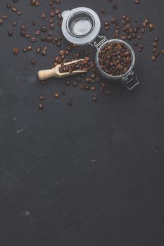Glass jar with roasted beans and wooden scoop on black stone concrete textured surface background. Top view with copy space for your text.