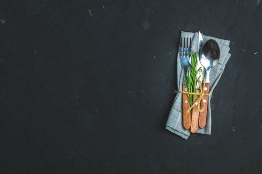Rustic vintage set of cutlery knife, spoon, fork. Black stone concrete surface background. Top view, copy space.