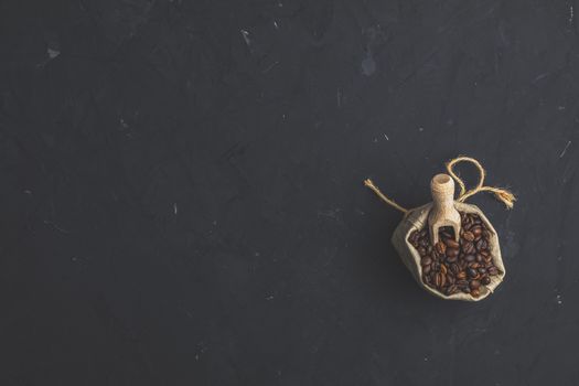 Purse with roasted beans and wooden scoop on black stone concrete textured surface background. Top view with copy space for your text.