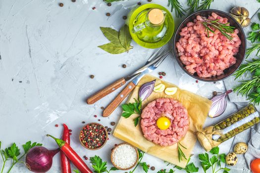 Healthy food, cooking concept. Homemade raw organic minced beef meat and steak tartare with yolk with vegetables on light gray stone concrete textured surface background. Copy space background, top view flat lay.