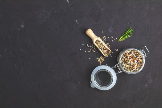 Black, purple, and white rice (Oryza sativa) mix in glass jar on black stone concrete textured surface background. Top view with copy space for your text.