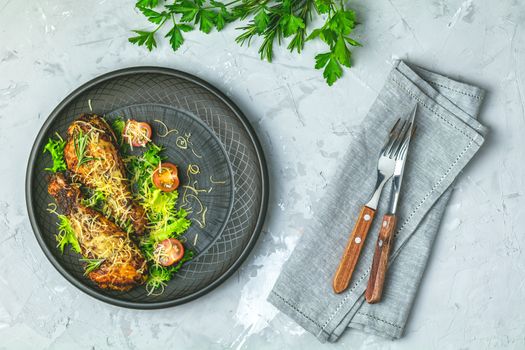 Baked chicken drumstick in a black ceramic plate with orange and rosemary, light gray stone concrete surface, top view, copy space.