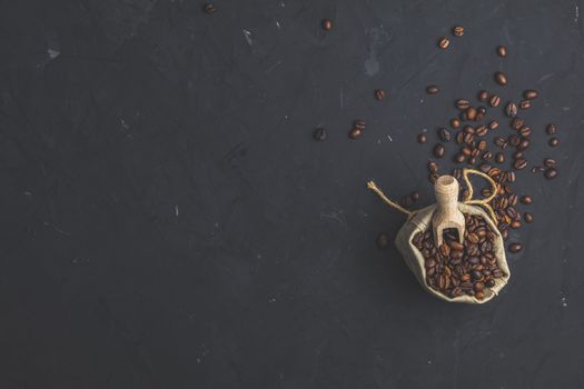 Purse with roasted beans and wooden scoop on black stone concrete textured surface background. Top view with copy space for your text.