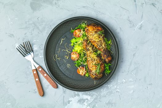 Baked chicken drumstick in a black ceramic plate with orange and rosemary, light gray stone concrete surface, top view, copy space.