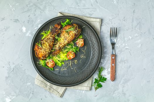 Baked chicken drumstick in a black ceramic plate with orange and rosemary, light gray stone concrete surface, top view, copy space.