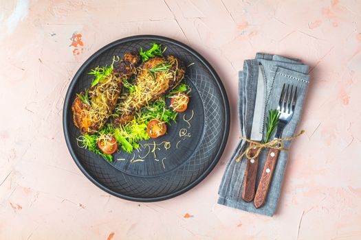 Baked chicken drumstick in a black ceramic plate with orange and rosemary, light pink living coral stone concrete surface, top view, copy space.