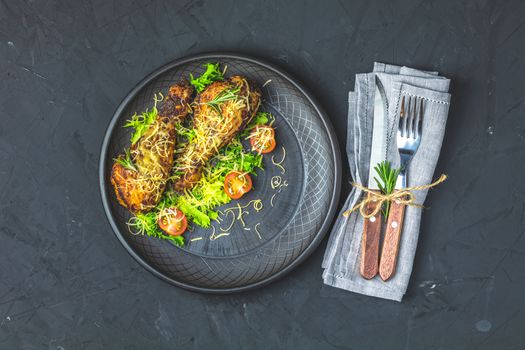 Baked chicken drumstick in a black ceramic plate with orange and rosemary, black stone concrete surface, top view, copy space.