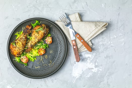 Baked chicken drumstick in a black ceramic plate with tomatoes and rosemary, light gray stone concrete surface, top view, copy space.