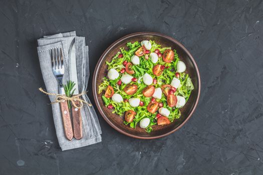 Fresh Cherry Tomato, Mozzarella salad with green lettuce mix served on a brown ceramic plate, healthy food, black stone concrete surface, top view, copy space.