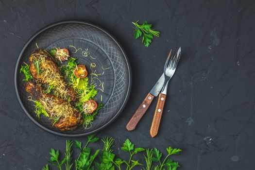 Baked chicken drumstick in a black ceramic plate with orange and rosemary, black stone concrete surface, top view, copy space.