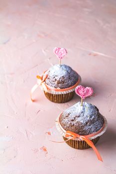 Tasty delicious homemade muffin on light pink living coral stone concrete surface with knitting hearts, copy space. Sweet food for valentines day.