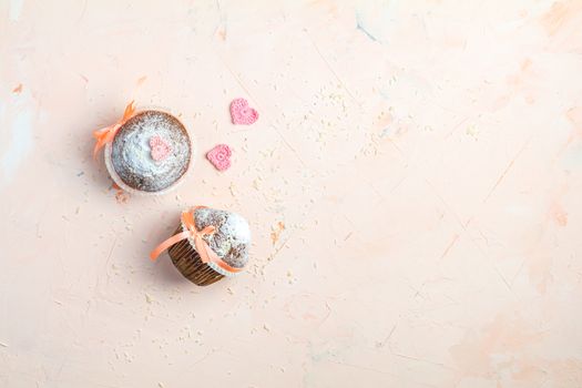 Tasty delicious homemade muffin on light pink living coral stone concrete surface with knitting hearts, top view, copy space. Sweet food for valentines dy.
