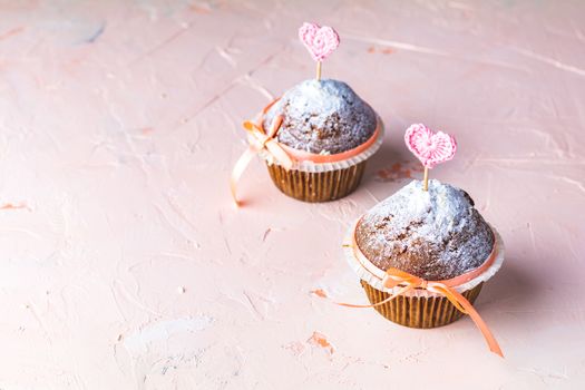 Tasty delicious homemade muffin on light pink living coral stone concrete surface with knitting hearts, copy space. Sweet food for valentines day.