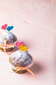 Tasty delicious homemade muffin on light pink living coral stone concrete surface with knitting hearts, copy space. Sweet food for valentines day.