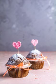 Tasty delicious homemade muffin on light pink living coral stone concrete surface with knitting hearts, copy space. Sweet food for valentines day.