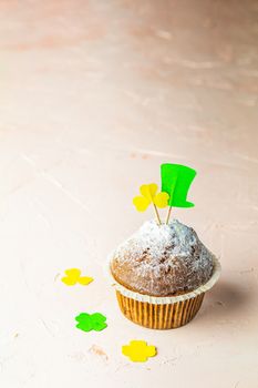 Tasty delicious homemade muffin on light pink living coral stone concrete surface with knitting hearts, copy space. Sweet food for Saint Patrick day.