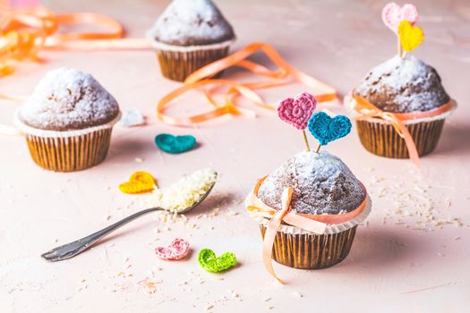 Tasty delicious homemade muffin on light pink living coral stone concrete surface with knitting hearts, copy space. Sweet food for valentines day.