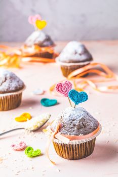 Tasty delicious homemade muffin on light pink living coral stone concrete surface with knitting hearts, copy space. Sweet food for valentines day.