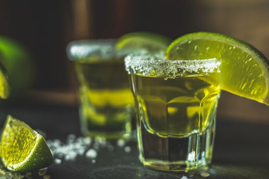 Mexican Gold Tequila shot with lime and salt on black stone table surface, selective focus, shallow depth of the field, copy space.