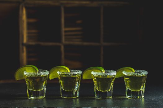 Mexican Gold Tequila shot with lime and salt on black stone table surface, selective focus, shallow depth of the field, copy space.