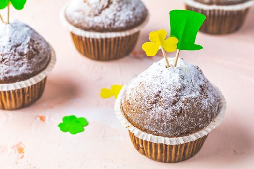 Tasty delicious homemade muffins on light pink living coral stone concrete surface with holiday attributes, copy space. Beautiful sweet food concept for Saint Patrick day.