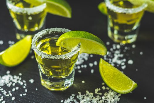 Mexican Gold Tequila shot with lime and salt on black stone table surface, selective focus, shallow depth of the field, copy space.