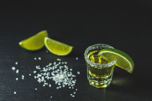 Mexican Gold Tequila shot with lime and salt on black stone table surface, selective focus, shallow depth of the field, copy space.