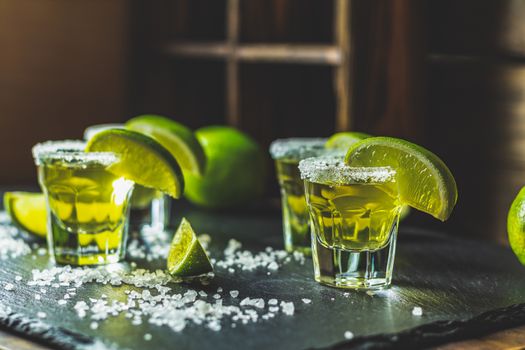 Mexican Gold Tequila shot with lime and salt on black stone table surface, selective focus, shallow depth of the field, copy space.