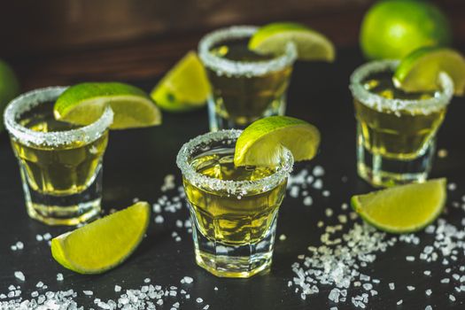 Mexican Gold Tequila shot  with lime and salt on black stone table surface, selective focus, shallow depth of the field, copy space.