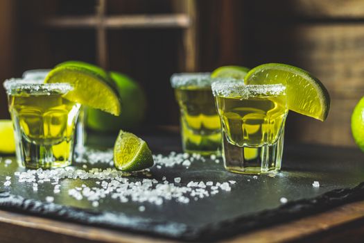 Mexican Gold Tequila shot with lime and salt on black stone table surface, selective focus, shallow depth of the field, copy space.