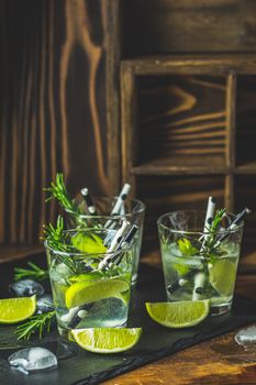 Fresh cocktail with lime, ice and rosemary, mojito cocktail in a bur on a rustic table, selective focus, shallow depth of the field.