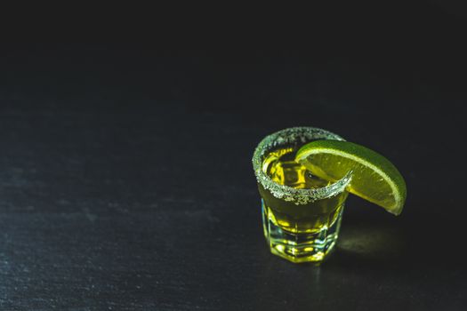 Mexican Gold Tequila shot with lime and salt on black stone table surface, selective focus, shallow depth of the field, copy space.