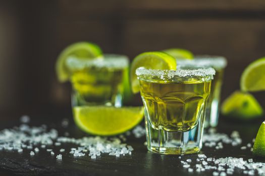 Mexican Gold Tequila shot  with lime and salt on black stone table surface, selective focus, shallow depth of the field, copy space.