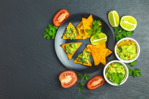 Guacamole and nachos with ingredients on the background of a black stone board. Top view, copy space.