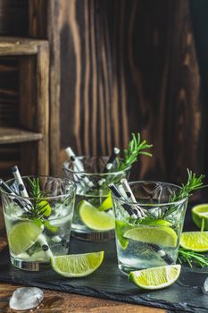 Fresh cocktail with lime, ice and rosemary, mojito cocktail in a bur on a rustic table, selective focus, shallow depth of the field.