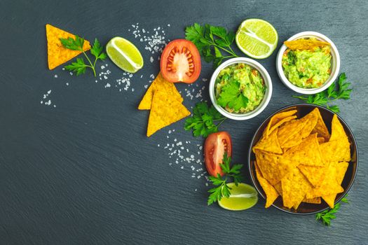 Guacamole and nachos with ingredients on the background of a black stone board. Top view, copy space.