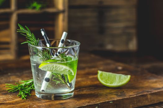 Fresh cocktail with lime, ice and rosemary, mojito cocktail in a bur on a rustic table, selective focus, shallow depth of the field.