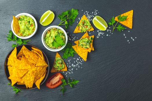 Guacamole and nachos with ingredients on the background of a black stone board. Top view, copy space.