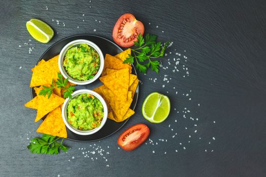 Guacamole and nachos with ingredients on the background of a black stone board. Top view, copy space.