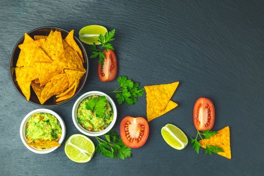 Guacamole and nachos with ingredients on the background of a black stone board. Top view, copy space.