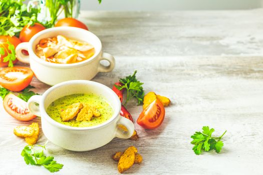 Concept of healthy vegetable and legume soups. Vegetables soup with carrot, eggs and chicken, mushroom cream soup with herbs and crackers and ingredients. Top view on the background of a light gray wooden board, copy space.