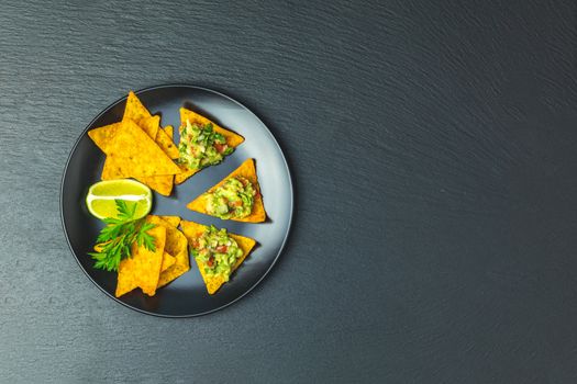 Guacamole and nachos with ingredients on the background of a black stone board. Top view, copy space.