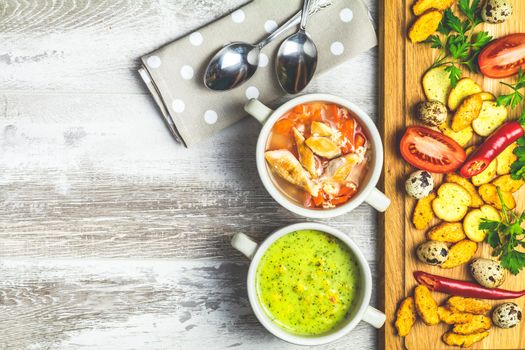 Concept of healthy vegetable and legume soups. Vegetables soup with carrot, eggs and chicken, mushroom cream soup with herbs and crackers and ingredients. Top view on the background of a light gray wooden board, copy space.