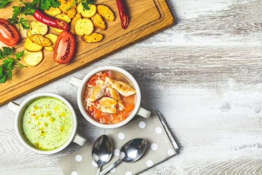 Concept of healthy vegetable and legume soups. Vegetables soup with carrot, eggs and chicken, mushroom cream soup with herbs and crackers. Top view, light gray wooden background, copy space