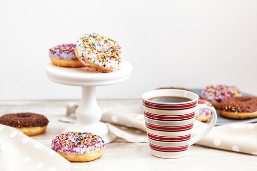 Delicious glazed donuts and cup of coffee on light wooden background. Beautiful romantic breakfast or lunch concept. Shallow depth of the field.