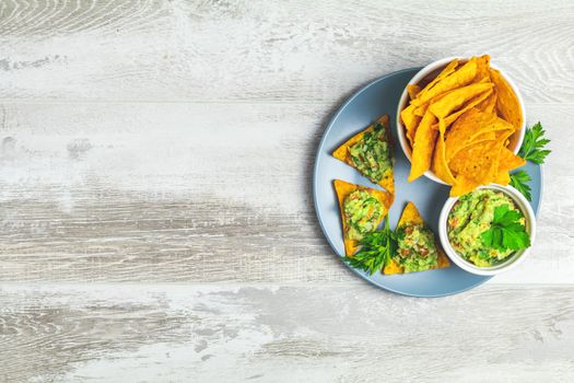 Guacamole and nachos with ingredients on the background of a light gray wooden board. Top view, copy space.