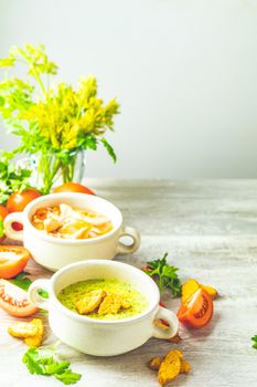 Concept of healthy vegetable and legume soups. Vegetables soup with carrot, eggs and chicken, mushroom cream soup with herbs and crackers and ingredients. Background of a light gray board, copy space