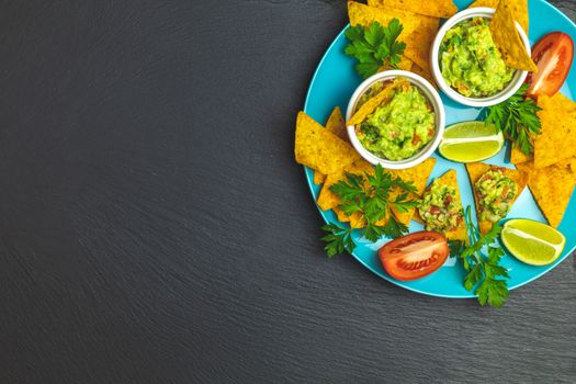 Guacamole and nachos with ingredients on the background of a black stone board. Top view, copy space.